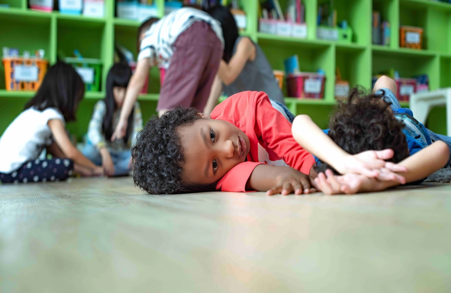 Young child lying on a classroom floor with a teacher kneeling beside them