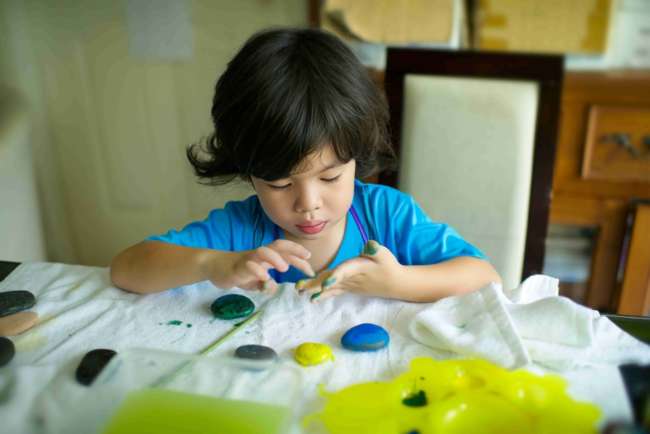 Cute Asian boy finger-painting on stones and paper