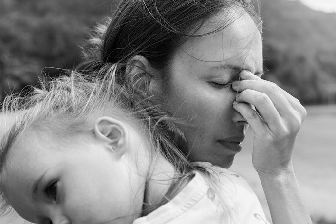 Black and white photo of a stressed mother holding her head with a young child nearby