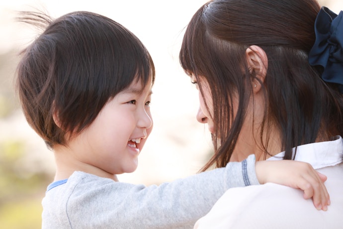 Young child smiling and looking up at a woman from behind