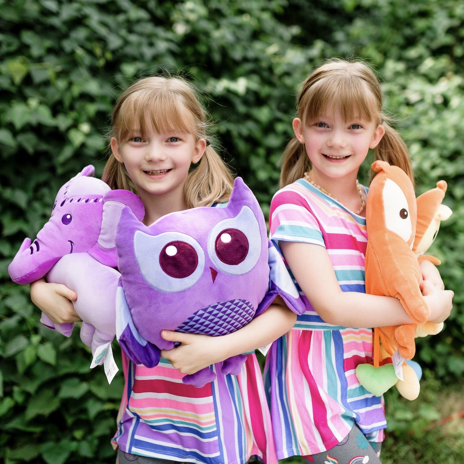 Two girls smiling outdoors each holding SnuggleBuddies emotions plush toys