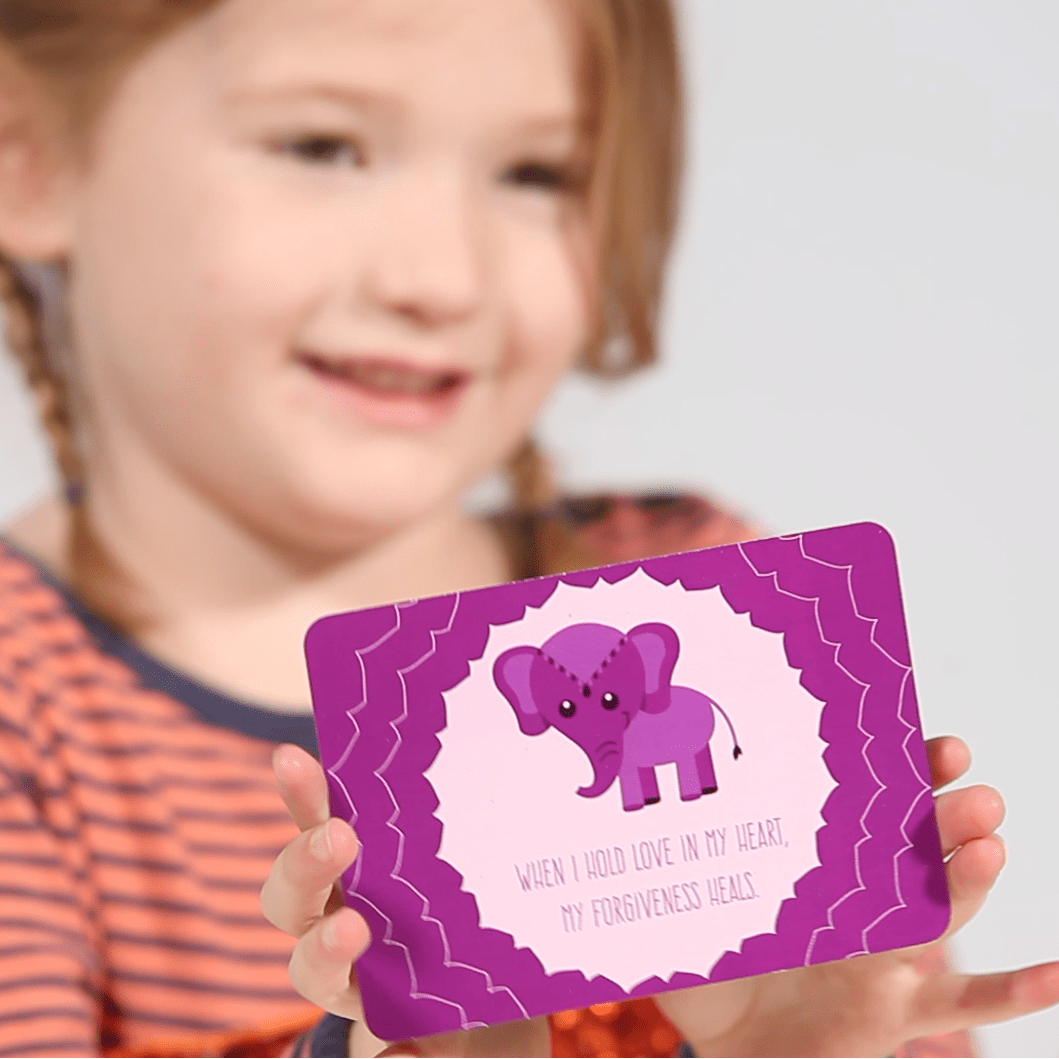 Smiling girl holding a purple PeaceMakers affirmation card with an elephant and forgiveness message